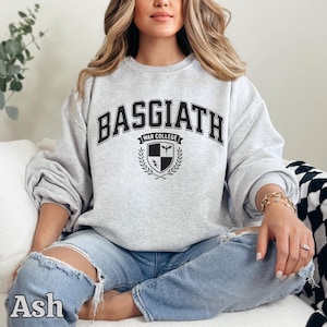 Peut inclure: Sweat-shirt gris clair avec l'inscription "BASGIATH WAR COLLEGE" en lettres noires. En dessous, un &eacute;cusson avec un bouclier, une &eacute;p&eacute;e et des branches de laurier. Le mot "Ash" est imprim&eacute; en bas &agrave; gauche.