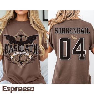 K&ouml;nnte beinhalten: Espressofarbenes T-Shirt mit einem Front-Grafikdesign, das einen Drachen und den Text "BASGIATH WAR COLLEGE" zeigt. Auf der R&uuml;ckseite des Shirts steht "SORRENGAIL" &uuml;ber der Nummer "04" in einem schwarz-wei&szlig;en Design. Das Shirt ist ein Freizeitartikel.