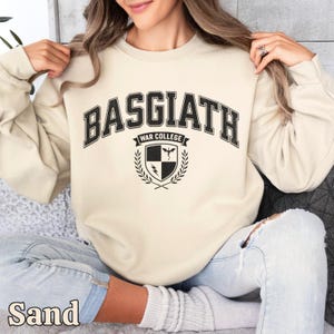 Peut inclure: Sweat-shirt couleur sable avec l'inscription "BASGIATH WAR COLLEGE" en noir. En dessous, un &eacute;cusson avec un bouclier, un &eacute;clair et une couronne de laurier. Le mot "Sand" est imprim&eacute; en bas.