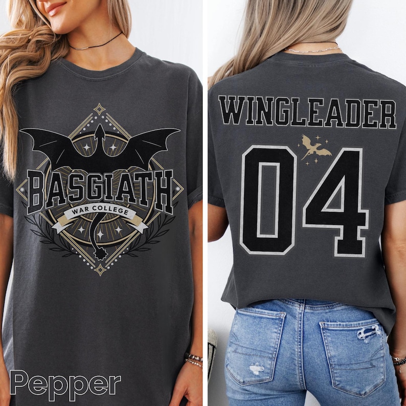 Op de afbeelding: Donkergrijs t-shirt met een drakenafbeelding en de tekst "BASGIATH WAR COLLEGE" op de voorkant. De achterkant van het shirt toont "WINGLEADER" en het nummer "04" in zwart en wit. Het shirt heeft een comfortabele pasvorm.