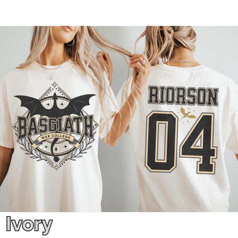 K&ouml;nnte beinhalten: Elfenbeinfarbene T-Shirts mit grafischen Designs. Eines zeigt "BASGIATH WAR COLLEGE" mit einem Drachenemblem. Das andere zeigt "RIORSON 04" mit einer kleinen Vogelgrafik. Die Shirts haben einen Rundhalsausschnitt und kurze &Auml;rmel.