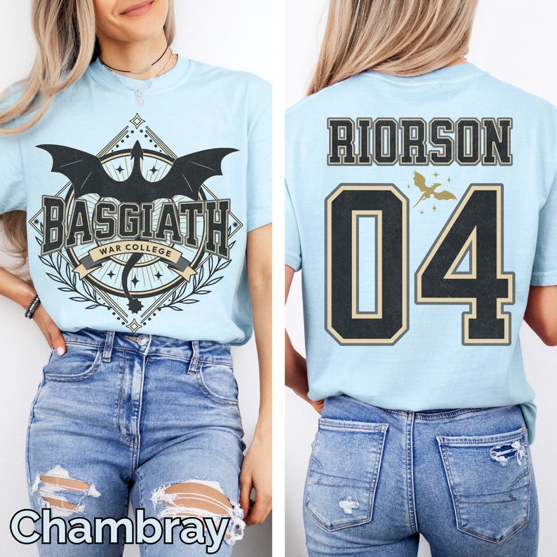 K&ouml;nnte beinhalten: Hellblaues T-Shirt mit einem Aufdruck auf der Vorderseite, der einen schwarzen Drachen, den Text "BASGIATH WAR COLLEGE" und einen dekorativen Rahmen zeigt. Auf der R&uuml;ckseite steht "RIORSON 04" in Schwarz und Gold. Das Wort "Chambray" steht unten.