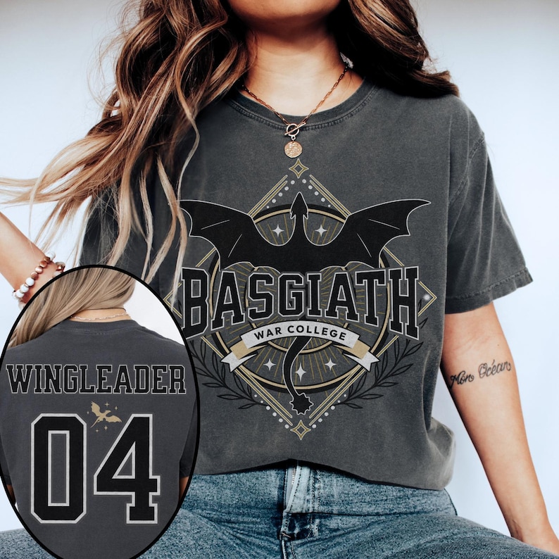 Vintage-style Basgiath War College tee inspired by Fourth Wing. Front features bold collegiate lettering with a bat-winged crest and star accents. Back shows customizable jersey-style design with ‘WINGLEADER’ and the number 04, plus a subtle golden dragon silhouette. Printed on a washed black Comfort Colors-style shirt for a soft, lived-in look. Perfect for fantasy fans and Riders Quadrant enthusiasts.
