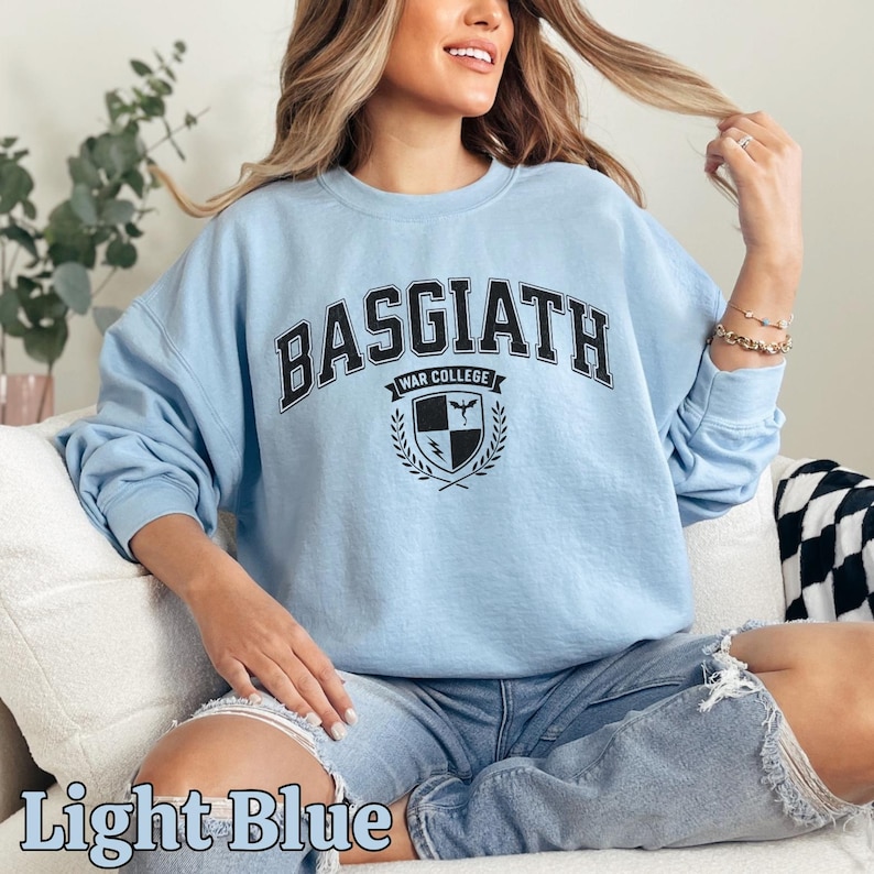 Peut inclure: Sweat-shirt bleu clair avec l'inscription "BASGIATH WAR COLLEGE" en noir. Le sweat-shirt a des manches longues et un col rond. Un &eacute;cusson est centr&eacute; sous le texte. Les mots "Light Blue" sont au bas de l'image.