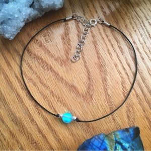 Puede incluir: Un delicado collar gargantilla con un colgante de orbe azul claro. El colgante est&aacute; adornado con cuentas plateadas y ensartado en un fino cord&oacute;n negro. El collar tiene un cierre de cadena ajustable plateado.