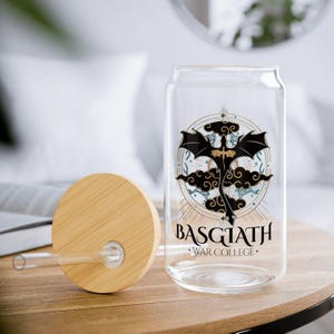 Puede incluir: Una botella de agua reutilizable de vidrio transparente con un diseño de dragón negro y dorado y el texto "Basgiath War College". La botella tiene una tapa de bambú con una pajita.