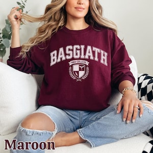 Peut inclure: Sweat-shirt bordeaux avec l'inscription blanche "BASGIATH WAR COLLEGE" et un &eacute;cusson. Le sweat-shirt &agrave; manches longues est de couleur unie. Le mot "Maroon" est imprim&eacute; en bas de l'image.