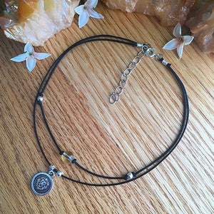 May include: A black cord choker necklace with a silver lion charm and a small amber bead. The necklace has a silver clasp.