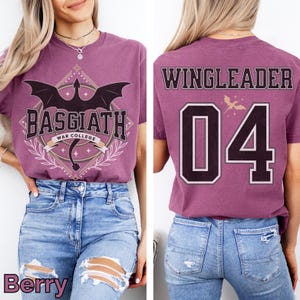 K&ouml;nnte beinhalten: Beerenfarbenes T-Shirt mit einem Aufdruck "BASGIATH WAR COLLEGE" und einer Drachenillustration. Auf der R&uuml;ckseite des Shirts steht "WINGLEADER 04". Das Shirt wird mit einer blauen Jeans kombiniert.