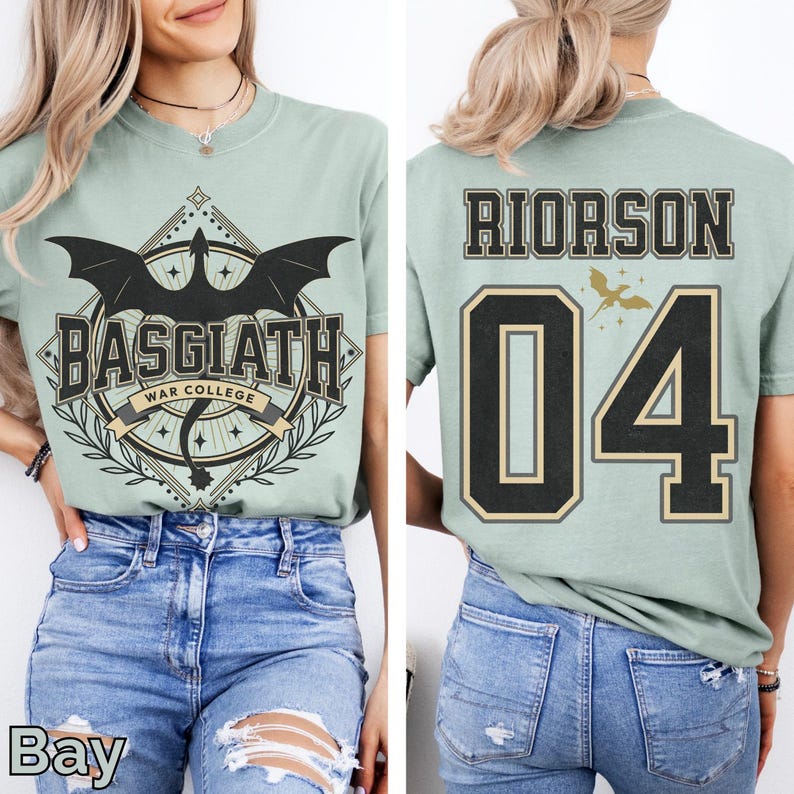 K&ouml;nnte beinhalten: Hellgr&uuml;nes T-Shirt mit dem Text "BASGIATH WAR COLLEGE" und einem Drachenmotiv auf der Vorderseite. Auf der R&uuml;ckseite des Shirts steht "RIORSON 04" in Schwarz und Gold. Das Shirt besteht aus einem weichen Material.