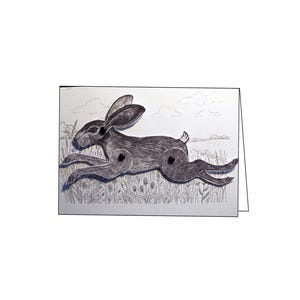 May include: A greeting card featuring a layered, articulated paper hare in a running pose. The hare is dark gray with black joints, set against a light background with a line-drawn illustration of a grassy meadow and a cloudy sky.