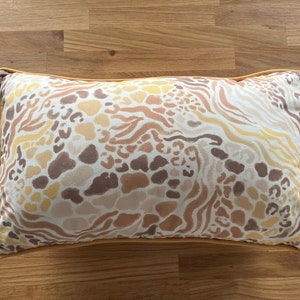 May include: A rectangular throw pillow with a brown, beige, and yellow abstract animal print pattern. The pillow has a yellow border.