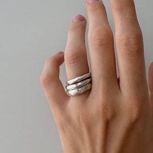 May include: A hand wearing three silver rings stacked on the ring finger. The hand has a black henna tattoo on the wrist.