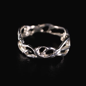 May include: A silver ring with an openwork design. The ring features a repeating pattern of intertwined shapes, creating a delicate and intricate appearance. The ring is set against a black background, highlighting its reflective surface.