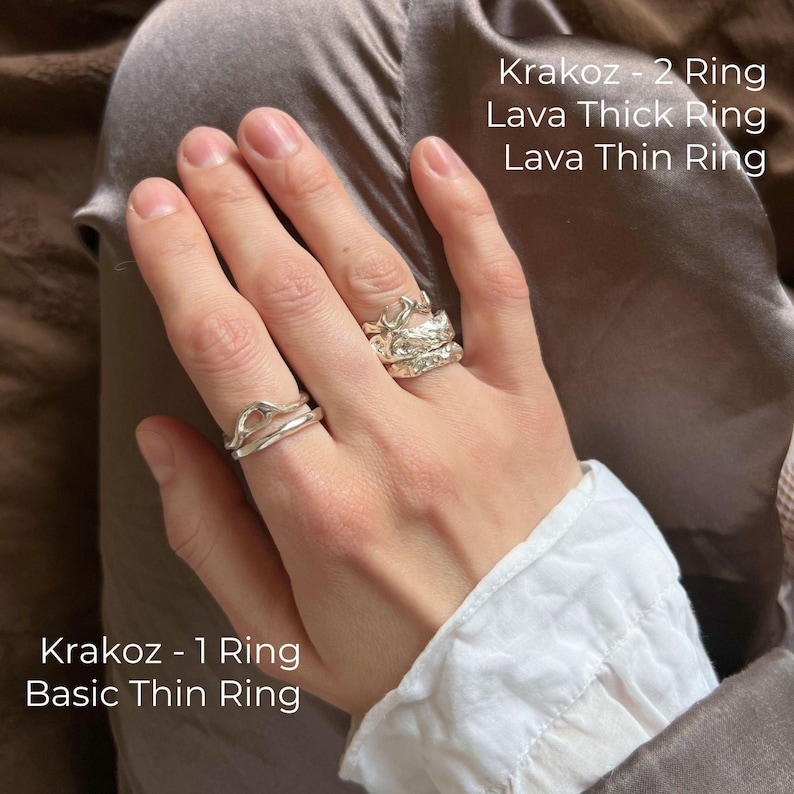 Close-up of a right hand wearing a funky rings stack and bold rings set with sterling silver ring designs. On the index finger, quirky wave ring and pointer finger ring layered as stacking ring with liquid molten ring and organic melted ring style. On the ring finger, edgy rings and abstract ring form a weird rings stack with silver funky rings and edgy weird rings aesthetic. Artsy pack of rings in alternative jewelry style, combining irregular wave ring, molten thin ring, and chunky silver ring