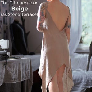 A woman wearing a beige dress with a tattoo on her arm stands in a room with a sewing machine and other sewing-related items visible.