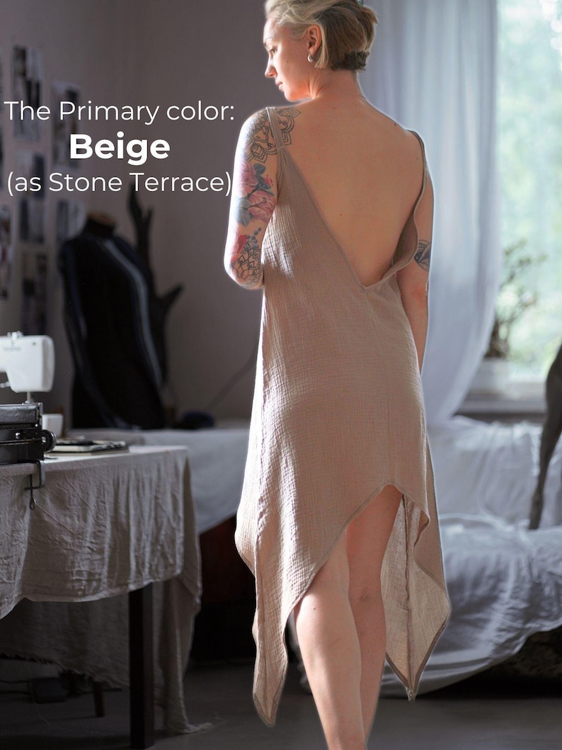 A woman wearing a beige dress with a tattoo on her arm stands in a room with a sewing machine and other sewing-related items visible.