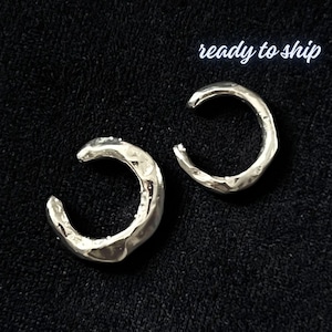 May include: Two silver-colored ear cuffs with a textured, organic design. The ear cuffs are crescent-shaped and sit against a black background. The text "ready to ship" is written in white script above the ear cuffs.