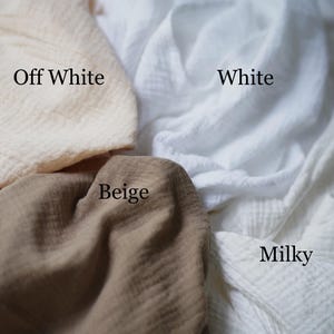 May include: Close-up of four swatches of fabric in different colors: off-white, white, beige, and milky. The fabric appears to be a soft, textured material. The names of the colors are written on the fabric.