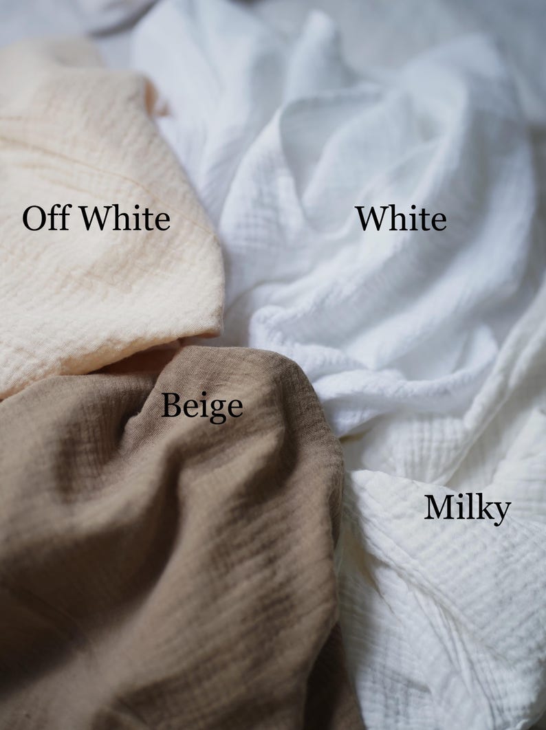 May include: Close-up of four swatches of fabric in different colors: off-white, white, beige, and milky. The fabric appears to be a soft, textured material. The names of the colors are written on the fabric.