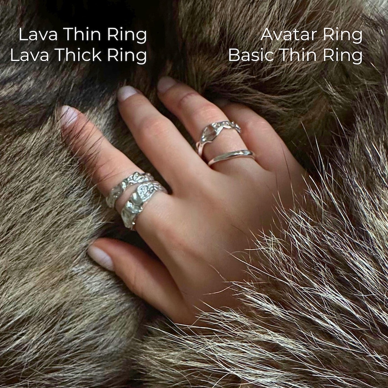 Close-up of a hand adorned with four handcrafted silver rings — Lava Thin Ring, Lava Thick Ring, Avatar Ring, and Basic Thin Ring — resting on natural wolf fur. Each ring features a unique texture, from organic molten patterns to minimalist curves. Text labels on the image identify the names of each ring, styled together in a bold stacked look.