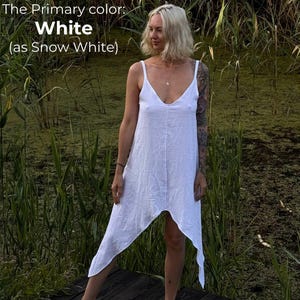 A woman in a white dress stands on a wooden platform in a natural setting, surrounded by tall grass and plants.