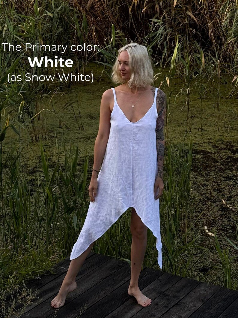 A woman in a white dress stands on a wooden platform in a natural setting, surrounded by tall grass and plants.