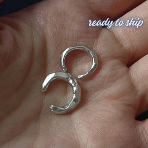 May include: A silver-colored earring with a unique, abstract design. The earring has a curved, crescent-like shape connected to a circular element. The text "ready to ship" is visible in the image.