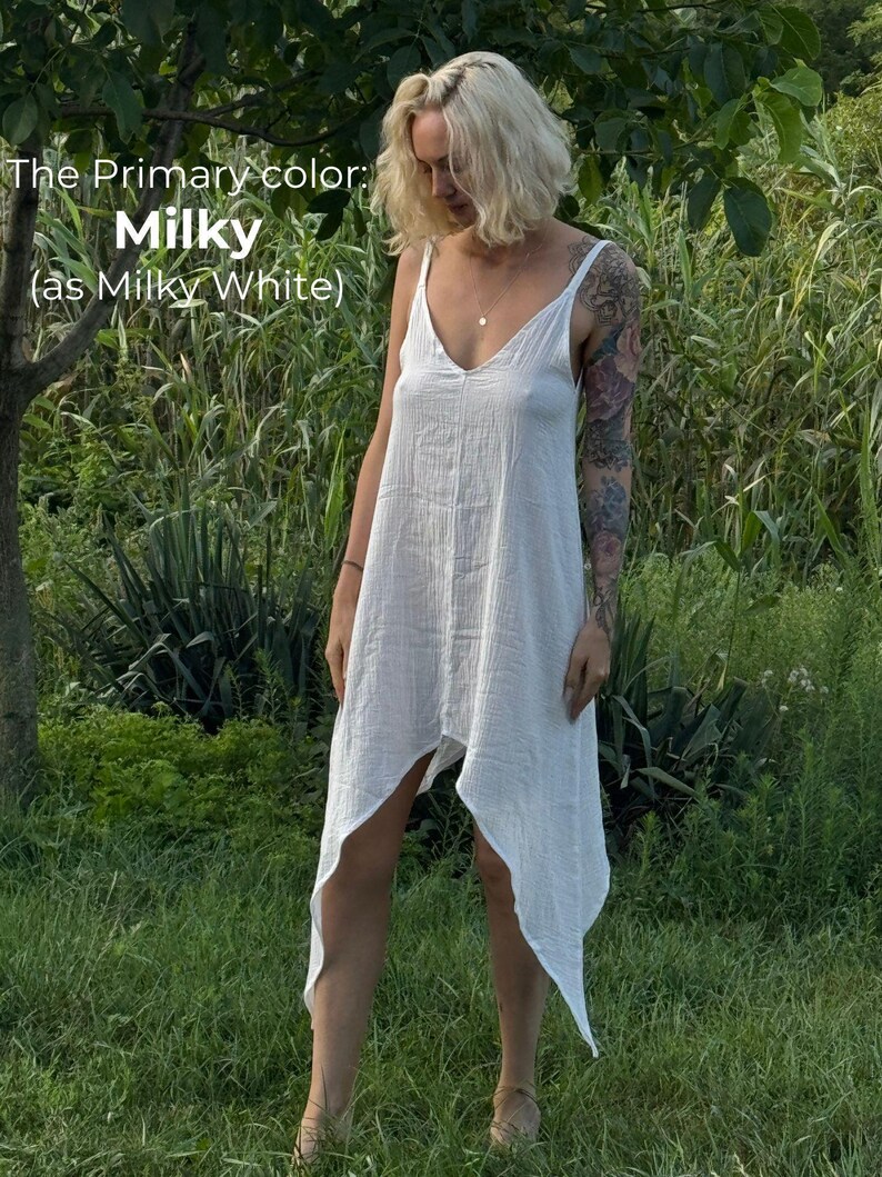 A woman in a white dress stands in a grassy field, surrounded by greenery.