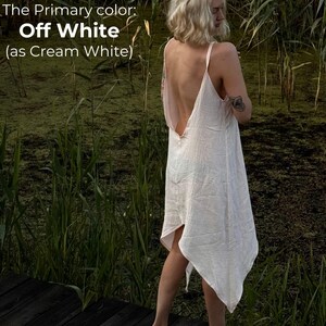 A woman in a white dress stands on a wooden boardwalk, surrounded by tall grass and reeds, with a text overlay describing the color of the dress as "Off White" as "as Cream White".