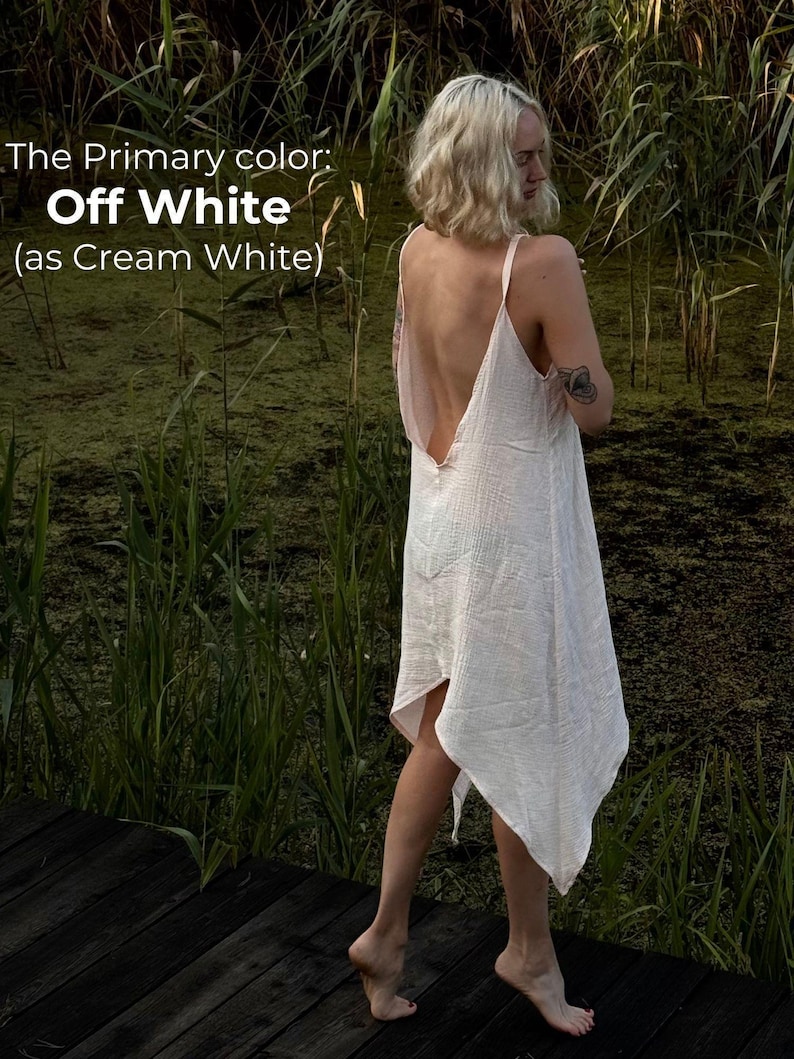 A woman in a white dress stands on a wooden boardwalk, surrounded by tall grass and reeds, with a text overlay describing the color of the dress as "Off White" as "as Cream White".