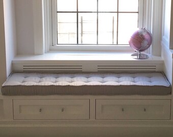 Puede incluir: Un asiento de ventana blanco con un cojín gris y dos cajones blancos. Un globo terráqueo rosa se encuentra en el alféizar de la ventana.