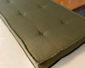 Puede incluir: Un cojín rectangular verde con capitoné de botones y un borde cosido.