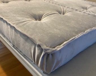 Puede incluir: Primer plano de un cojín gris claro capitoné con un diseño capitoné de botones. El cojín tiene una tela gruesa y suave y un borde bien definido.