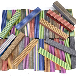 May include: A collection of colorful wooden blanks with striped patterns. The blanks are arranged in a random pattern and are ready to be turned into pens, pencils, or other crafts.