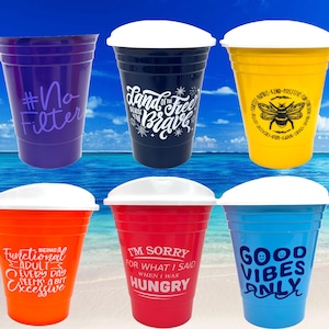 May include: Six colorful plastic cups with white lids and various humorous sayings printed on them. The sayings include "#No Filter", "Land of the Free Because of the Brave", "Being a Functional Adult Every Day Seems a Bit Excessive", "I'm Sorry for What I Said When I Was Hungry", "Good Vibes Only", and "Be Kind, Positive, Creative, Brave, Happy, Love, Give".