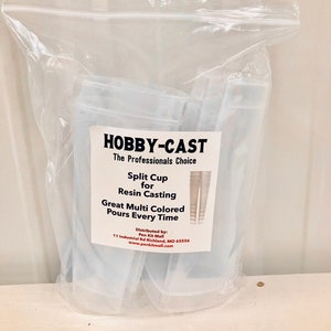 May include: A package of clear plastic split cups for resin casting. The package has a label that reads "HOBBY-CAST The Professionals Choice Split Cup for Resin Casting Great Multi Colored Pours Every Time Distributed by: Pen Kit Mall 11 Industrial Rd Richland, MO 65556 www.penkitmall.com"