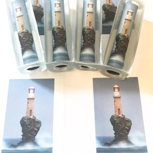 May include: Five clear glass cylinders with a lighthouse image inside. The lighthouse is on a rocky island with waves crashing around it. The cylinders are arranged in a row on a white surface.