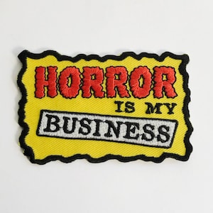 May include: Yellow embroidered patch with black outline. The patch says "HORROR IS MY BUSINESS" in black and red lettering.