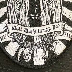 May include: Black and white embroidered patch with a skull and crossbones, a chain, and a banner that reads "What Would Lemmy Do?"