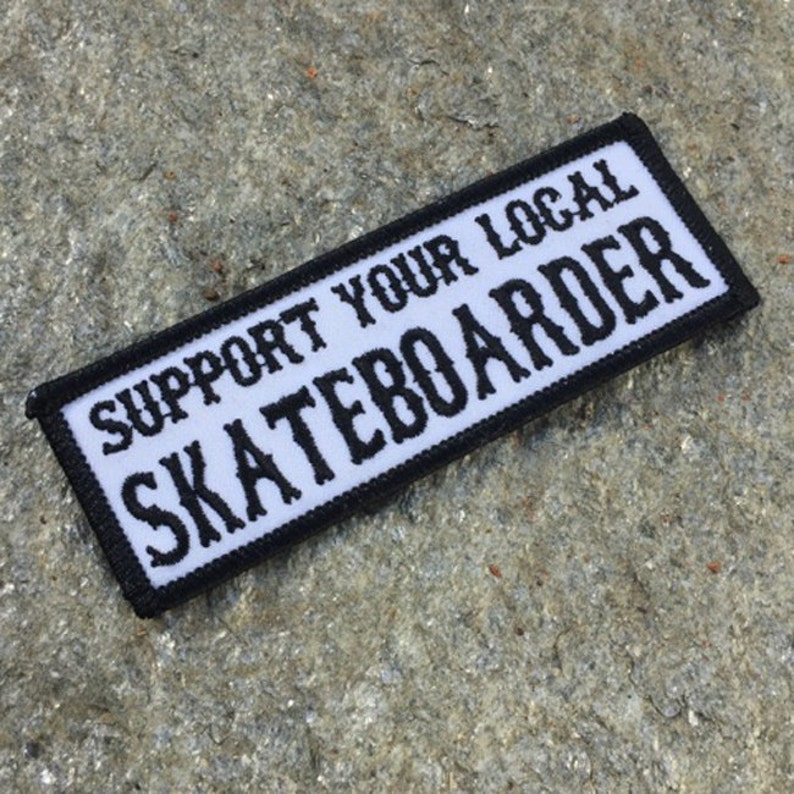 May include: White patch with black border and text that reads "Support your local skateboarder".
