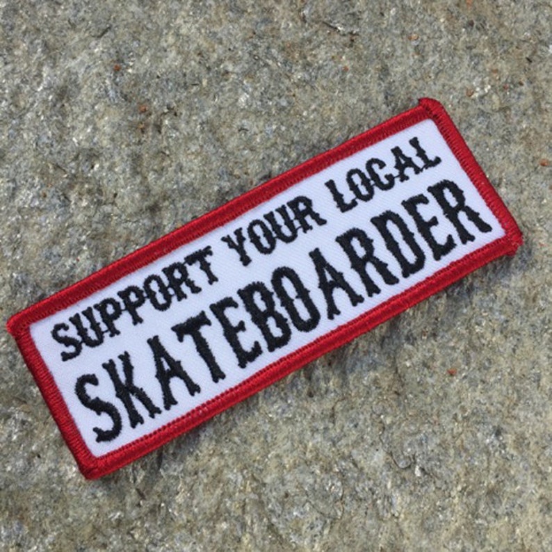 May include: White patch with red border, featuring the text "SUPPORT YOUR LOCAL SKATEBOARDER" in black lettering.
