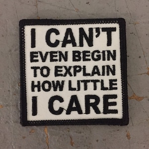 May include: White square patch with black embroidered text that reads "I CAN'T EVEN BEGIN TO EXPLAIN HOW LITTLE I CARE".
