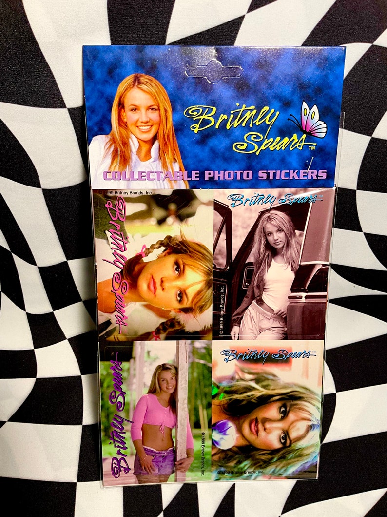 May include: Collectible photo stickers featuring images of Britney Spears. The packaging is blue with the singer's name in gold script and a butterfly graphic. The stickers showcase various photos of Spears.