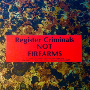 May include: A red rectangular sign with the text "Register Criminals NOT FIREARMS" in bold black letters. The sign also includes the text "Citizens Committee for the Right to Keep & Bear Arms" and an address. The background is a mottled pattern of brown, gold, and black.