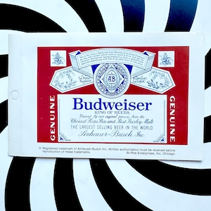 May include: A Budweiser beer label with a red background and white text. The label features the Budweiser logo, the words "King of Beers," and other text describing the beer's ingredients and brewing process. The label is rectangular.