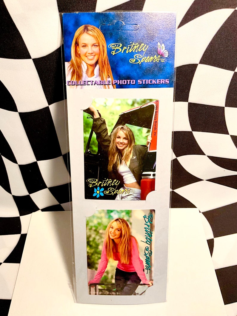 May include: Collectible photo stickers featuring Britney Spears. The packaging is blue and white, with images of Britney Spears in various poses. The text "Britney Spears" and "Collectible Photo Stickers" are visible.