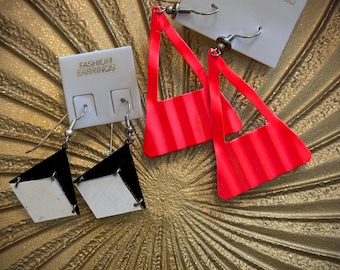 May include: Two pairs of vintage earrings on a gold-toned surface. One pair features black and white geometric shapes, while the other has bright red, striped triangle designs. The earring cards read "FASHION EARRINGS".
