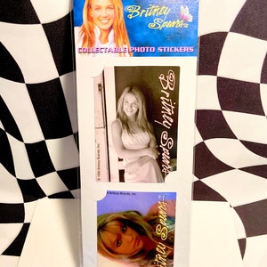May include: Collectible photo stickers featuring Britney Spears. The stickers have images of Britney Spears in various poses. The top of the package has a blue background with the text "Britney Spears" and "COLLECTABLE PHOTO STICKERS".