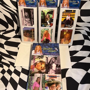May include: Collectible photo stickers featuring Britney Spears. The stickers are packaged in clear plastic with a blue and gold design. The stickers showcase various images of Britney Spears, with the text "Britney Spears" on each sticker.
